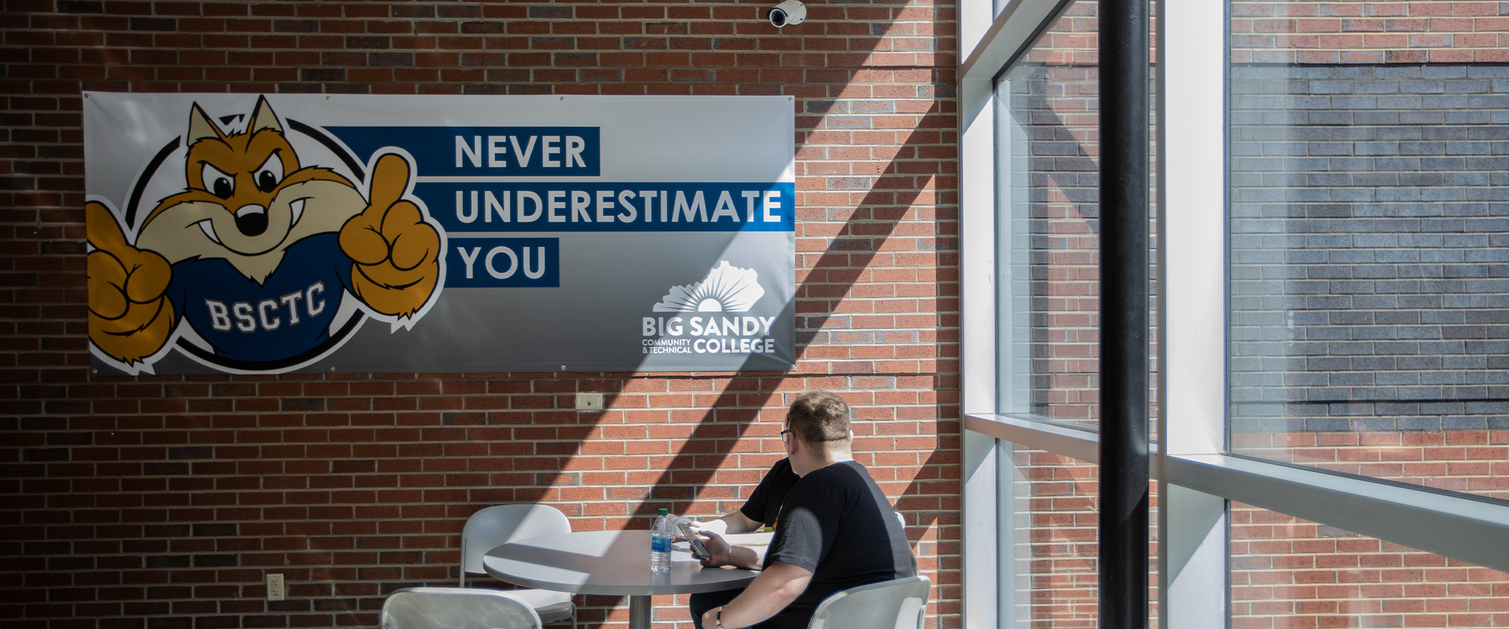 Students sitting in front of a campus sign that reads: Never Underestimate You