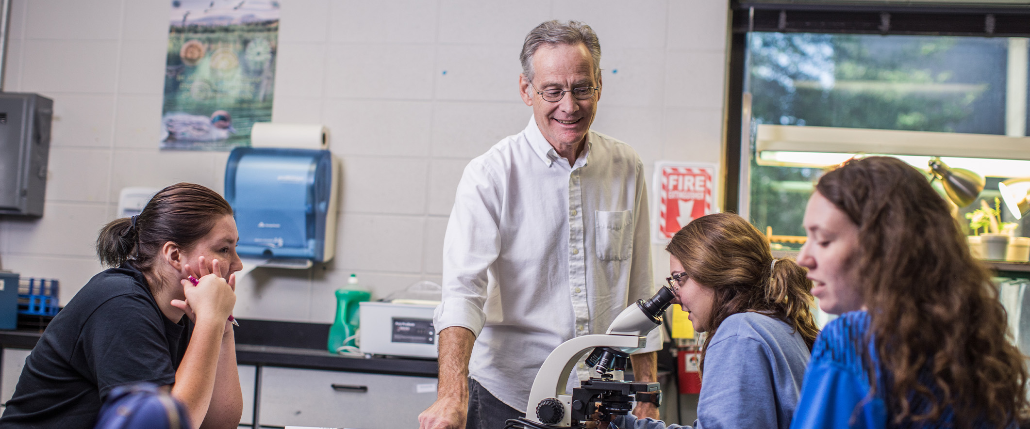 Science professor working with three students and a microscope in a classroom lab