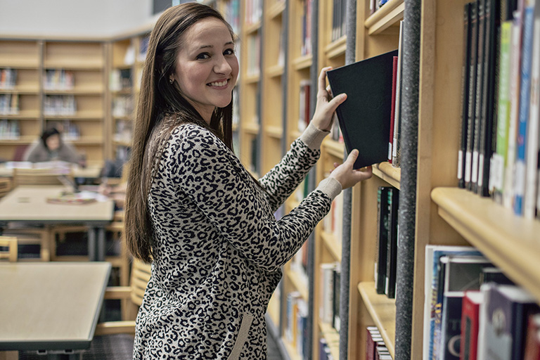 girl grabbing book off library shelf