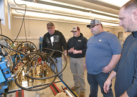 students and instructors examine an industrial bench covered in tubes and valves