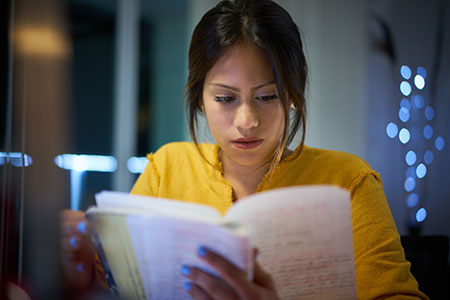 Woman studying a folded book at home in dim light.